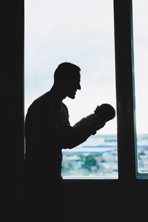 A young loving dad holds his son in his arms against the background of the window.の写真素材