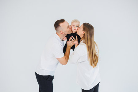 Young parents, a man and a woman, kiss their little son. A family couple with a child in their arms on a white background.の写真素材