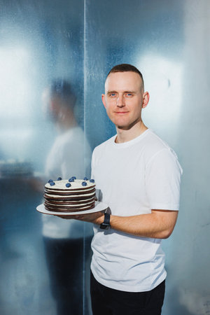 A young confectioner man holds a fresh sweet fruit cake in his hands. A man presents a cake.の写真素材