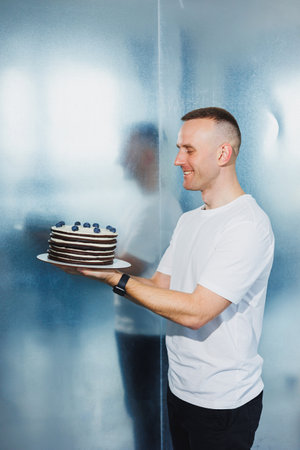 A young confectioner man holds a fresh sweet fruit cake in his hands. A man presents a cake.の写真素材