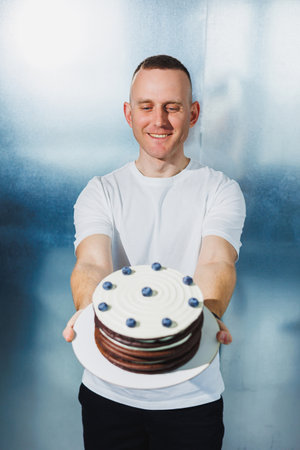 A young confectioner man holds a fresh sweet fruit cake in his hands. A man presents a cake.の写真素材