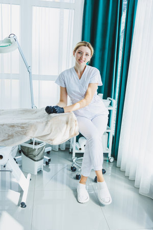 A young female doctor in a white medical suit is sitting in the office and waiting for a patient. Dermatologist's officeの写真素材