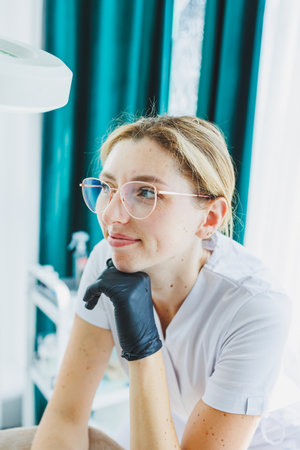 A young female doctor in a white medical suit is sitting in the office and waiting for a patient. Dermatologist's officeの写真素材