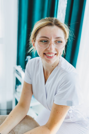 A young female doctor in a white medical suit is sitting in the office and waiting for a patient. Dermatologist's officeの写真素材