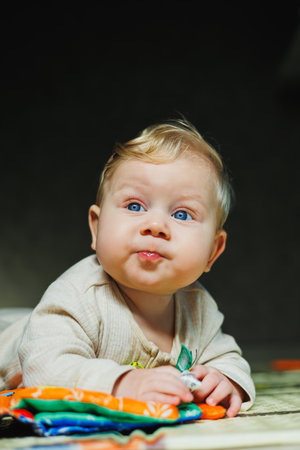 A small child in a white bodysuit is learning to crawl on a clean, heated floor. Home photo of a...