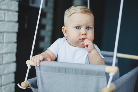 Baby boy swings on a swing at home. A child rides on a swing at homeの写真素材