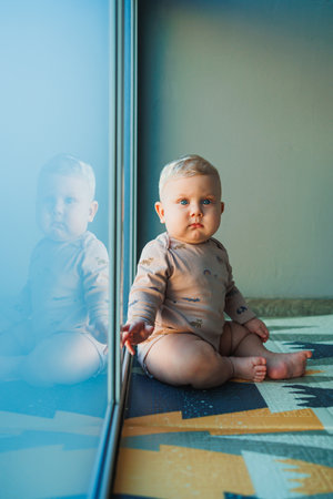 A baby boy tries to stand up by the window. The child learns to stand. Child development.の写真素材