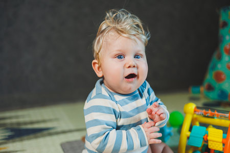 Cute blond baby toddler playing with baby toys at home sitting on carpet. Smiling cute little child...