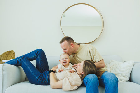 A young married couple is having fun playing with a small child in a modern living room together....