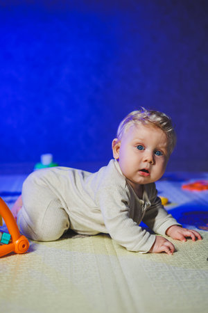 Little child, boy in bodysuit, playing with toys on rug at home in bright room, baby with blue eyes