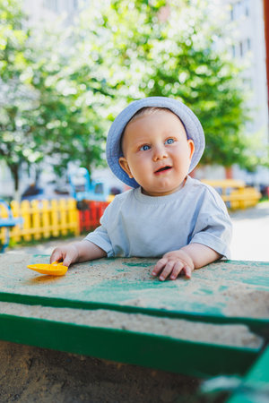 A little baby boy, 11 months old, in a t-shirt and a panama on his head, plays with sand on a summer day. A child is playing on the street.の写真素材