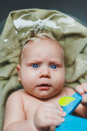 A fair-haired boy with blue eyes, a baby lies in a bathtub and bathes in water. Bathing the baby.の写真素材