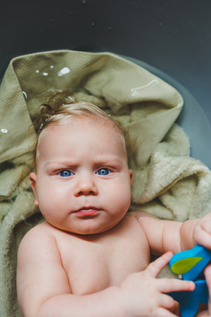 A fair-haired boy with blue eyes, a baby lies in a bathtub and bathes in water. Bathing the baby.
