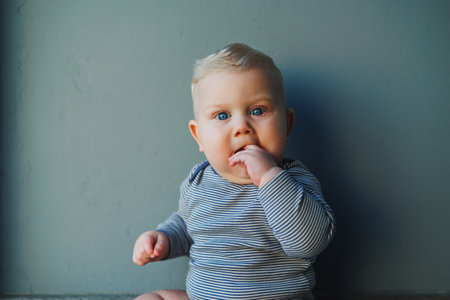 A blue-eyed fair-haired little boy in a bodysuit is crawling on the floor. Clothes for babies.の写真素材