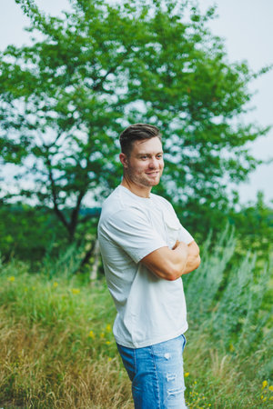 A handsome man in a white t-shirt stands in nature and breathes fresh air. Outdoor recreation....