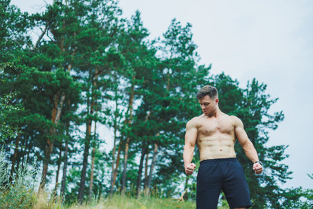 A young man with abs cubes on the background of the forest. Athletic pumped-up man on a rock background.の写真素材