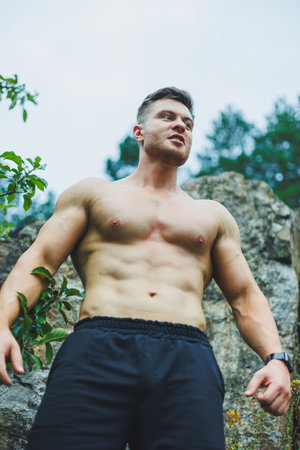 Toned shirtless muscular young man in sportswear showing abs outdoors in park.の写真素材