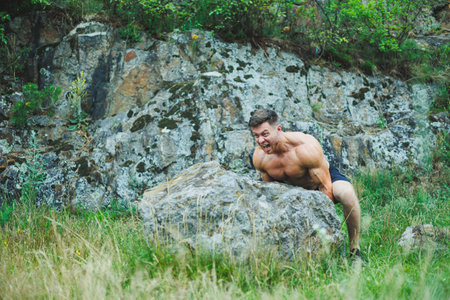 Photo of an athlete, a muscular, athletic young man doing exercises with a naked torso, in the forest, mountains.の写真素材