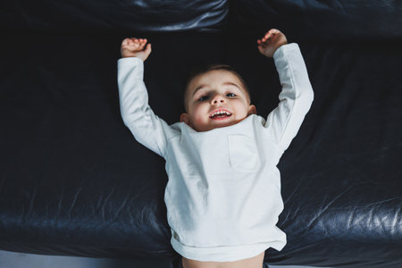 A 3-year-old boy in white raglan and gray pants is sitting on the couch. Stylish boy with a smile on his face. Clothes for boys.の写真素材