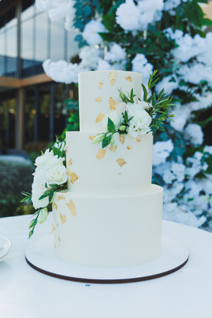 A sweet holiday cake on the background of a photo zone for the newlyweds. White multi-tiered cake.