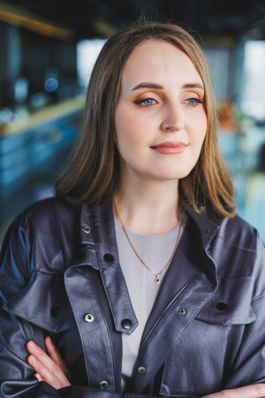 A woman in a leather jacket is standing in a cafe. Beautiful girl in casual clothes.