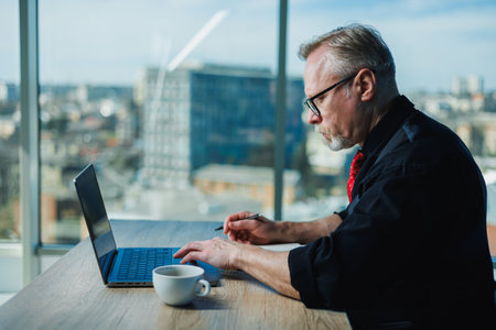 Gray-haired stylish freelancer man, gray-haired businessman at workplace in office. Adult bearded...