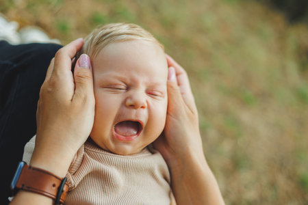 Close-up of a little boy's face with a smile. Child's emotions. A young mother holds her little son in her arms while standing in the park.の写真素材