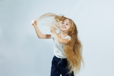 Young beautiful girl with long curly hair in jeans and a white t-shirt on a white background. Different emotions on the girl's face.の写真素材