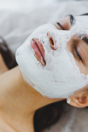 Skin care for a woman's face. A woman with a white mask on her face is lying on a beautician's...