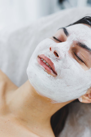 Close-up of a woman's face with a white mask on her face. Mask on the face of your client in the beauty salon. Skin cleansing and moisturizing concept. Facial skin care.の写真素材
