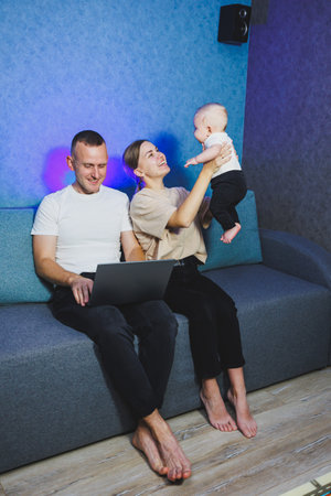 Young married couple having fun playing with cute little baby in modern living room together. Smiling parents, mom and dad, enjoying spending time with their son at homeの写真素材