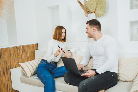 A man and a woman are sitting on the couch at home and watching a video on a laptop.の写真素材