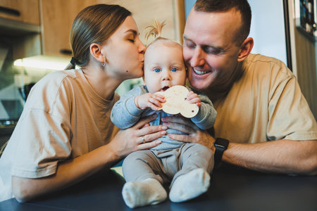 A young married couple with a small son in the kitchen. Parents hug their son.