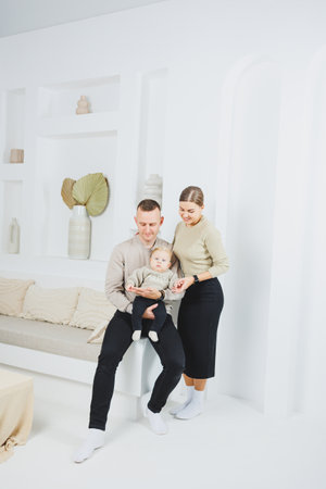 A family with a baby in their arms at home. Happy young family mom dad and newborn baby smiling and kissing on room background, loving family at homeの写真素材