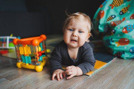 A blue-eyed baby lies on the floor and looks into the camera. A baby with white hair in a gray...