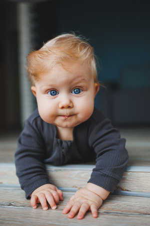 A blue-eyed baby lies on the floor and looks into the camera. A baby with white hair in a gray...