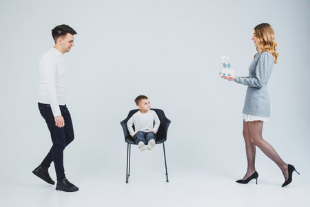 A happy married couple with a small son and a delicious cake in their hands. Mom dad and smiling son celebrating birthday. Stylish family.の写真素材
