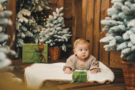 A baby on the background of a Christmas tree with a wrapped gift. A child at home against the...