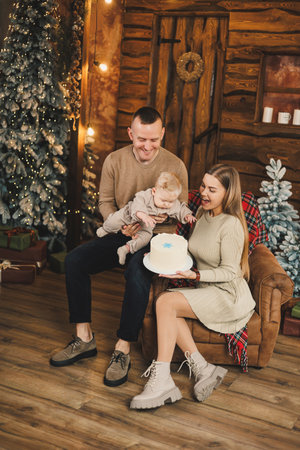 A happy young family with a small child is celebrating the new year near the Christmas tree in a bright house, kissing and hugging. New Year in the circle of the family.の写真素材