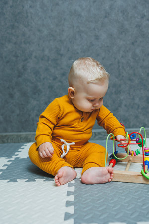 A baby in a bodysuit sits on the floor and plays with educational toys. Toys for the development of...