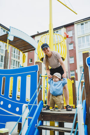 A mother teaches her son to walk, the first steps of a baby. The child walks holding his mother's hand. A baby in a hoodie and shorts on a walk. clothes for baby boys.の写真素材
