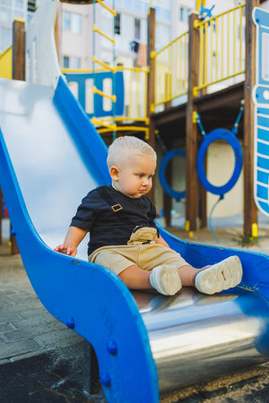 A 1-year-old boy goes down a hill on the playground outside. A baby is playing outdoors. Child development.の写真素材