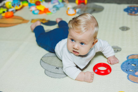 A little six-month-old boy is learning to lie on his stomach. The baby plays with toys lying on the...