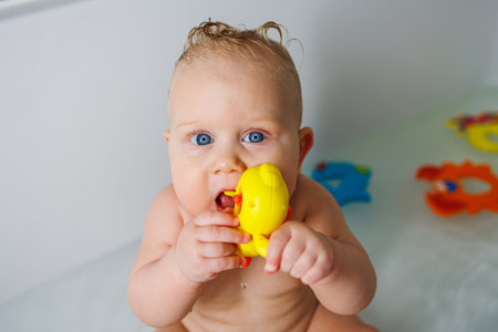 A smiling baby is standing in a white bath with water. Baby bathing in water. Personal hygiene of...