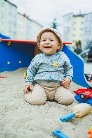 Cheerful baby boy playing with sand sitting on the playground. Children's games in the fresh air....