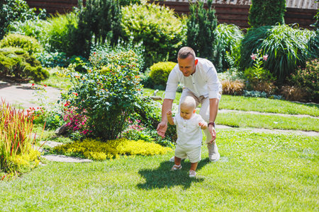 Smiling dad walks with his little son in nature. A boy in a white shirt and shorts. Holiday clothes for boys.の写真素材