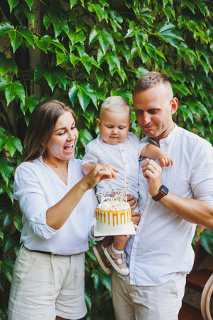 Mom and dad in nature with their one-year-old son celebrate his first birthday with a cake. Birthday...