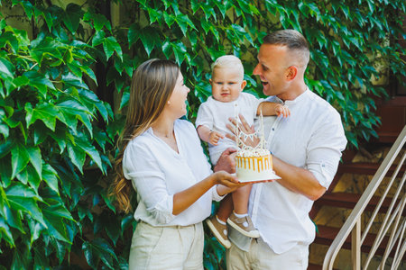 Mom and dad in nature with their one-year-old son celebrate his first birthday with a cake. Birthday with a cake in nature.の写真素材