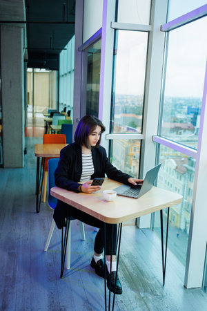 A young woman wearing glasses is sitting in a modern spacious working office. Woman office worker...