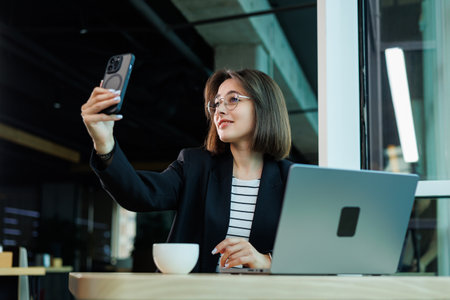 A young woman wearing glasses is sitting in a modern spacious working office. Woman office worker with laptop working.の写真素材